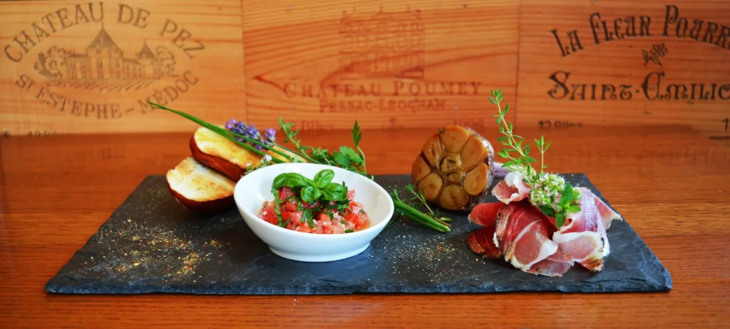 Bruschette de tomates, jambon cru San Daniele et ail confit, dressés sur ardoise.